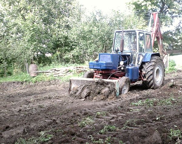 Трактор снимает плодородный слой на участке
